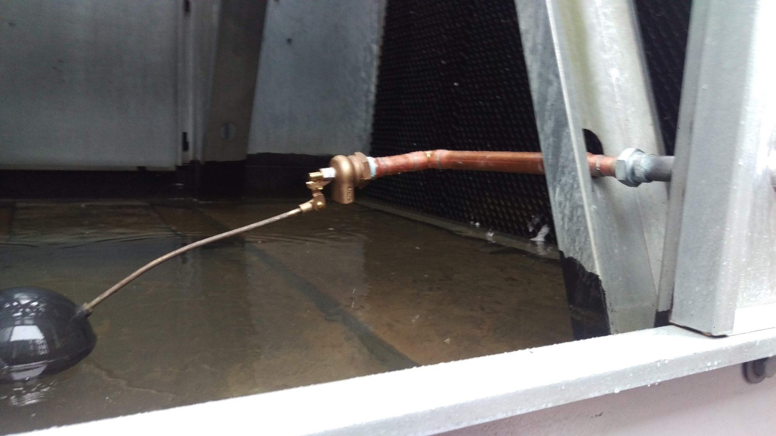 Mechanical float valve and copper supply line inside the cooling tower basin for makeup water level control.